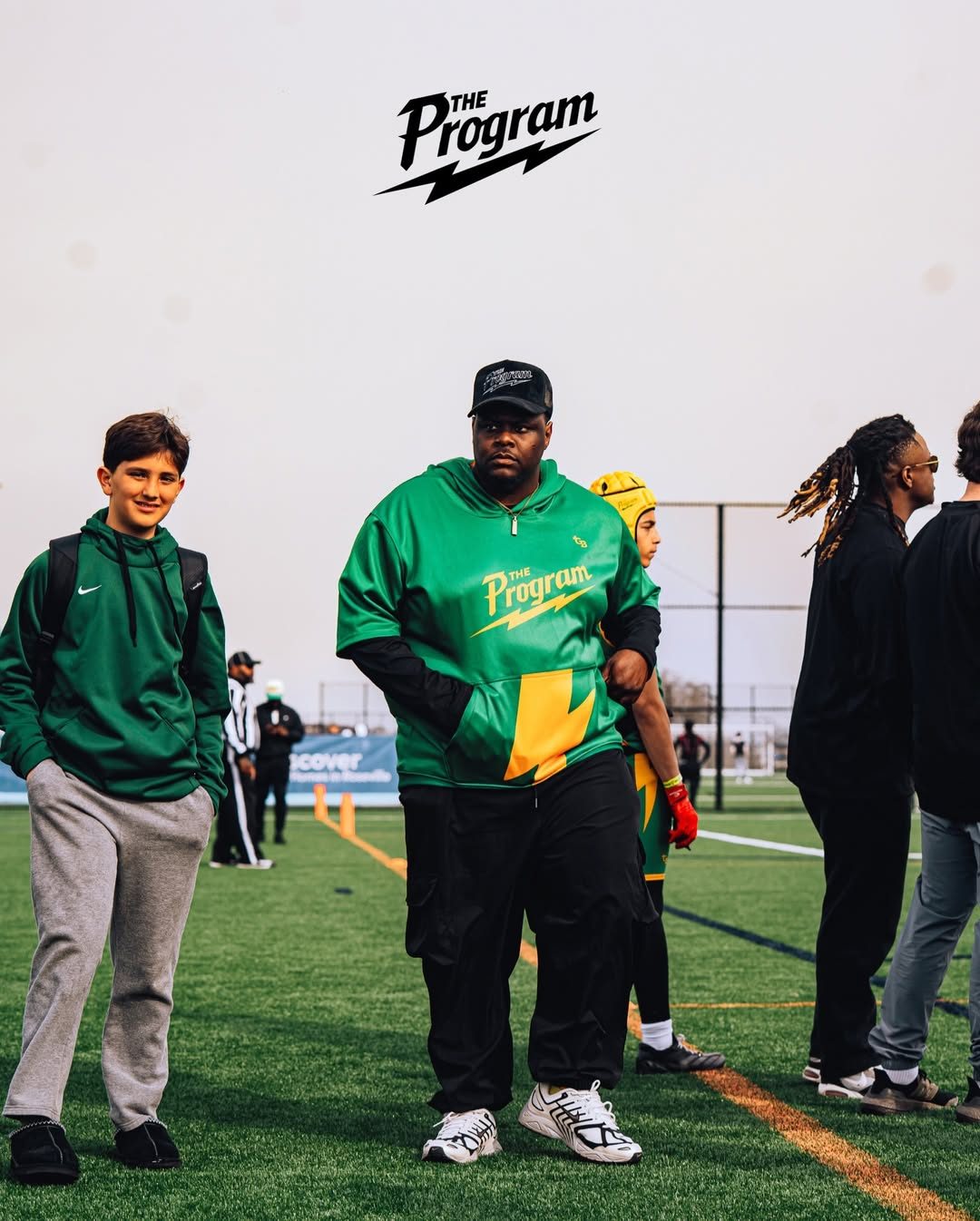 A Program coach in the green and yellow kit walking the sideline