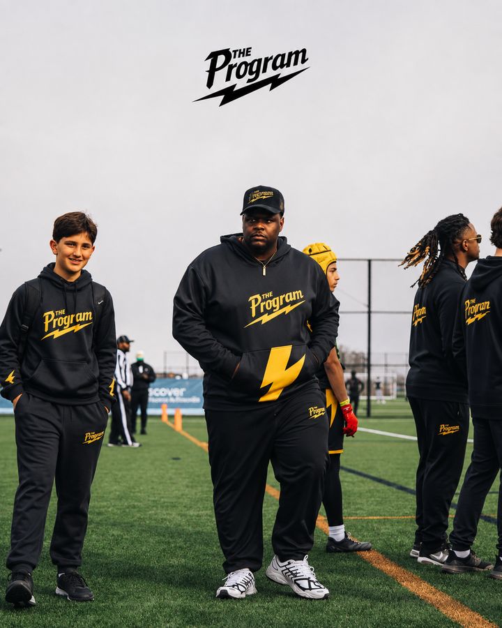 A Program coach walking the sideline with athletes in blackout kit