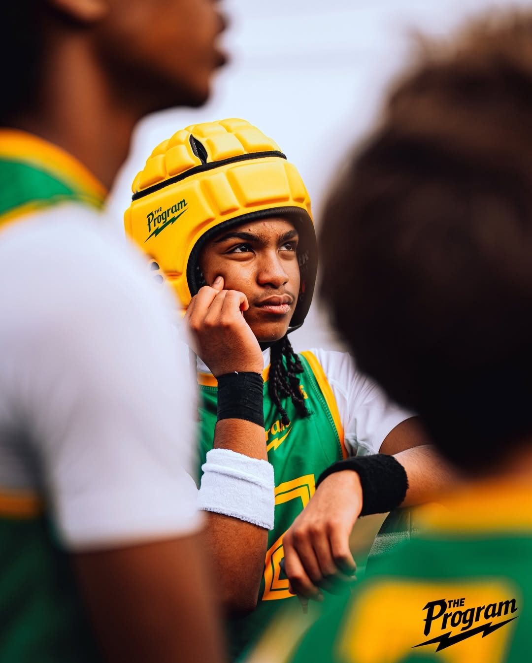 Program athlete in green kit and yellow headgear listening in the huddle
