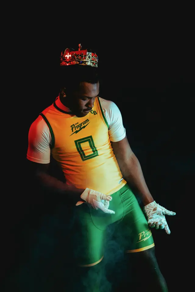 Crowned Program athlete kneeling with the ball at his shoulder, green socks glowing