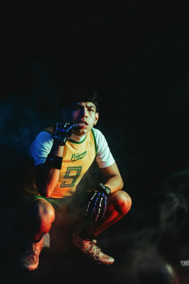 Program athlete number 9 crouched, biting a skeleton-print glove