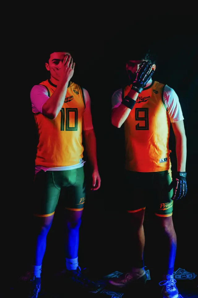 Two Program athletes in gold jerseys covering their faces under red and blue studio light
